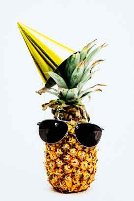 photo of pineapple wearing black aviator style sunglasses and party hat